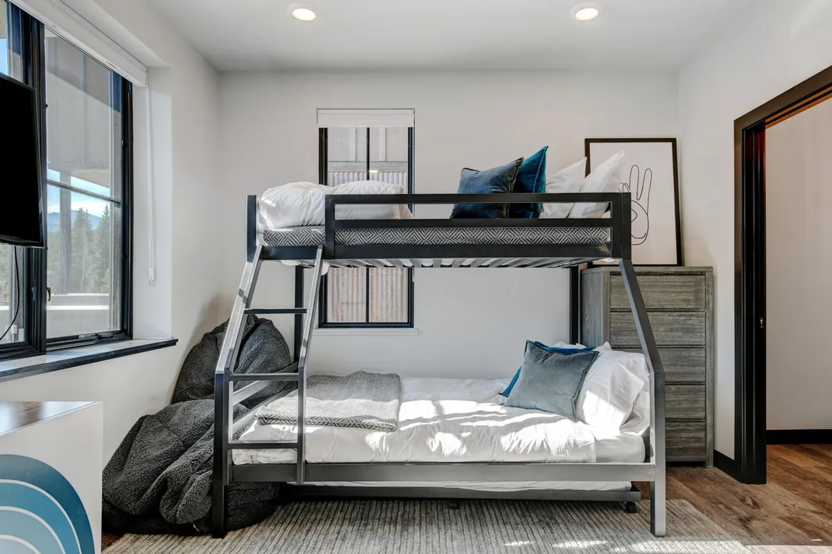 A bright, playful bunkroom with a bunk bed, bean bag chairs, decorative artwork, and a dresser. The space feels open and fun, ideal for sleepovers, reading, or playing games, and suited to groups or families with kids.