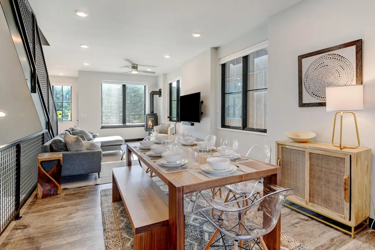 An open-concept dining and living area set for a meal, featuring a cozy dining table, comfortable seating area, modern décor, and a large window inviting in natural light. The space exudes warmth and readiness for both intimate dinners and larger celebrations.