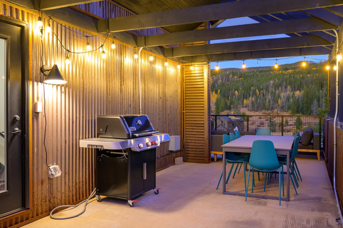 A cozy outdoor dining area featuring a grill and a dining table set beneath string lights, with a stunning mountain view in the background. The scene is inviting and intimate, ideal for celebrating special occasions or gathering with friends under the stars.