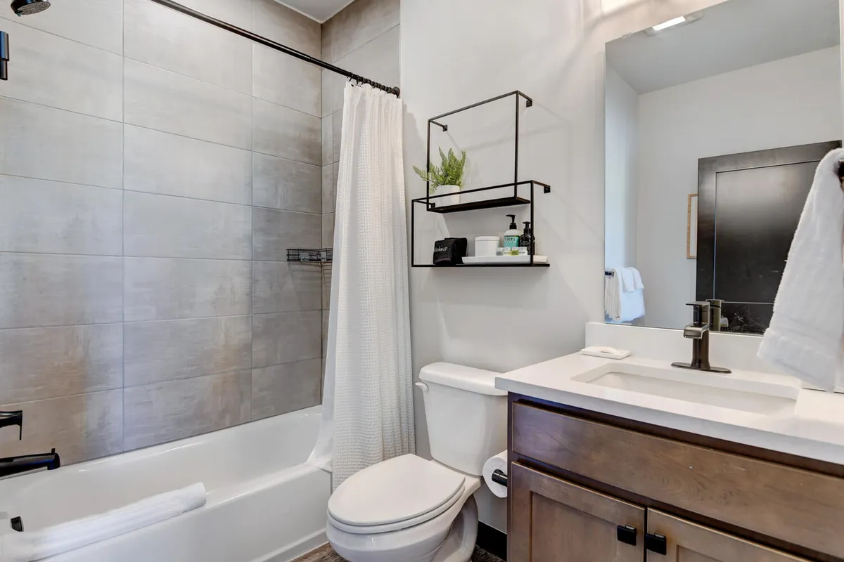 A modern bathroom with a relaxing bathtub, sleek sink, shelf with greenery, and a large mirror. The setting feels tranquil and inviting—an ideal spot for self-care routines or unwinding after a long day.