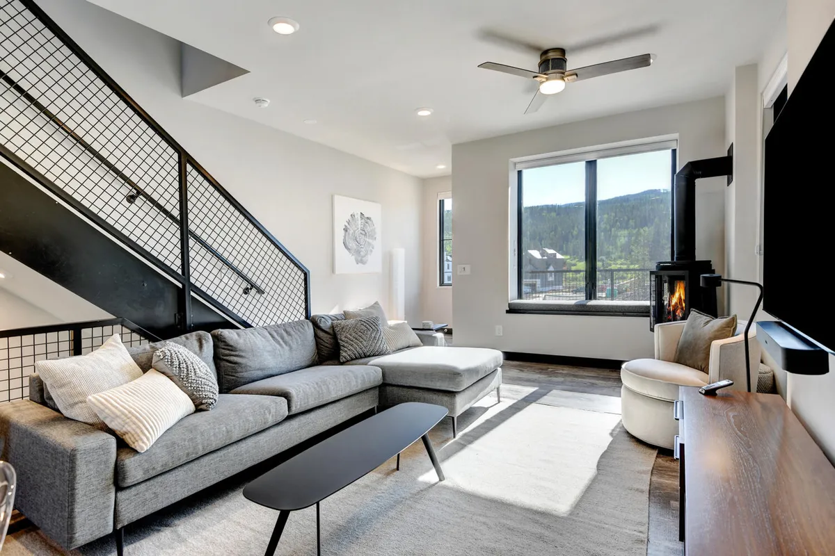 A contemporary living room with a stylish sofa, coffee table, custom stone fireplace, and a large window with an inviting view. The setup encourages relaxation and socializing, with a cozy ambiance for enjoying a movie night or warming up après-ski.