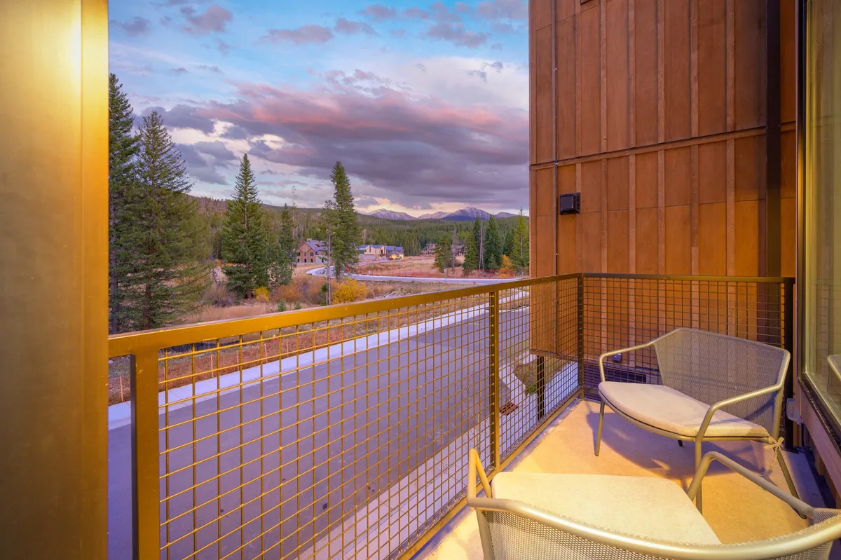 An exterior view from a balcony with chairs, overlooking expansive mountain scenery. The scene is tranquil, bathed in evening light, suggesting a perfect spot to unwind and enjoy the outdoors with your pet after a day of adventure.