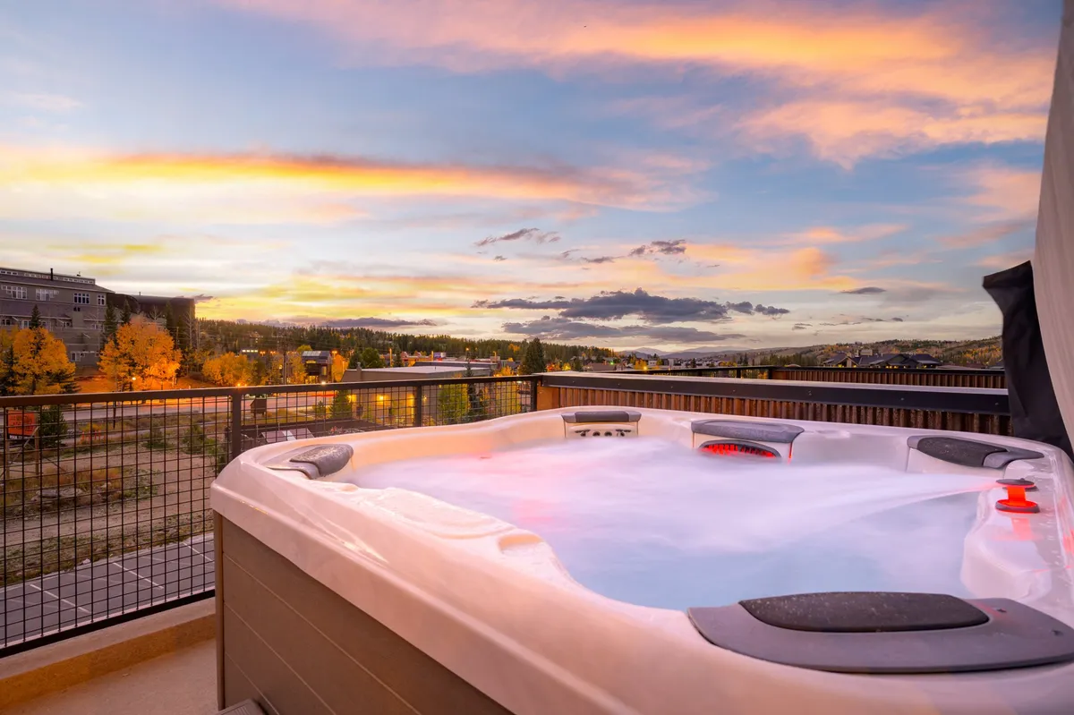 A serene rooftop hot tub takes center stage, set against a dramatic sunset and expansive horizon. The scene exudes relaxation, with soft lighting and a sense of privacy, allowing guests to soak while soaking in sweeping mountain views.