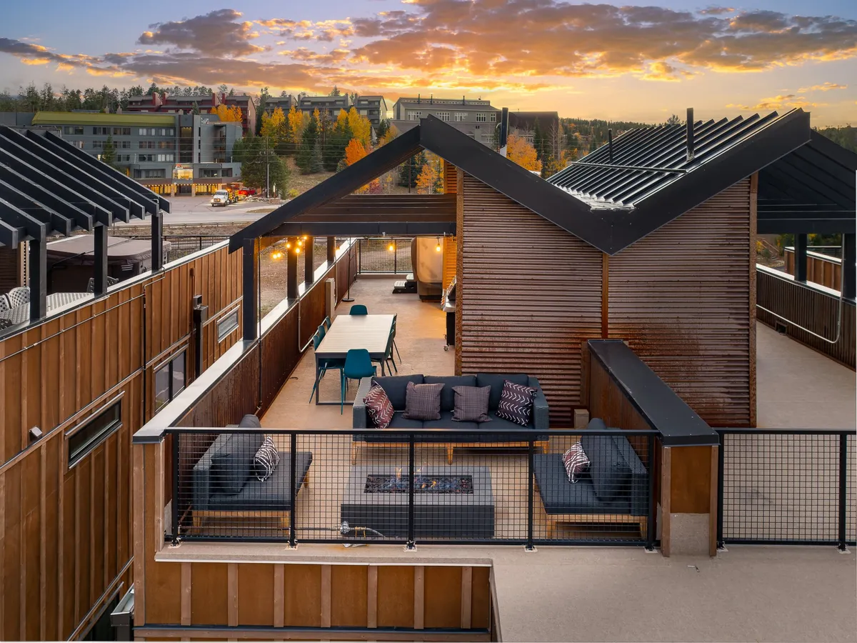 Contemporary outdoor furniture and a spacious dining table are arranged on a terrace, with a scenic background of trees and a vibrant sunset sky. The atmosphere is relaxed yet sophisticated, ideal for brunches and sunset cocktails.
