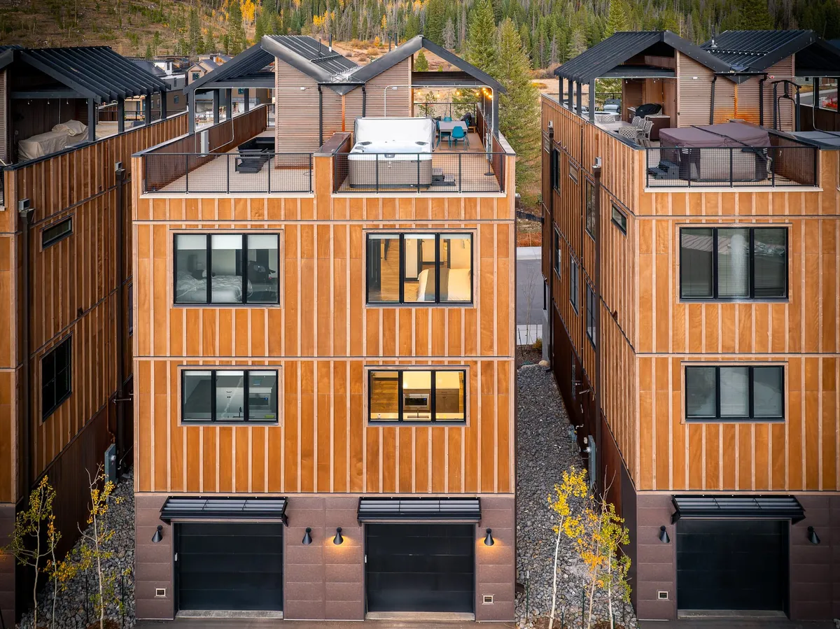 A modern wooden facade with a rooftop deck featuring outdoor seating and a hot tub, set against a mountain backdrop. The deck is designed for relaxation, stargazing, and entertaining guests, emphasizing a seamless blend of luxury and nature.
